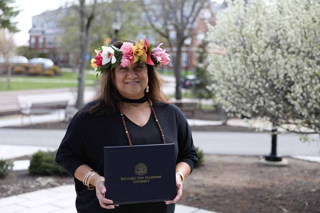 Sharla Kaleihua Kahale-Miner自豪地穿着夏威夷花环头上,握着她的文凭,以SNHU校园为背景。