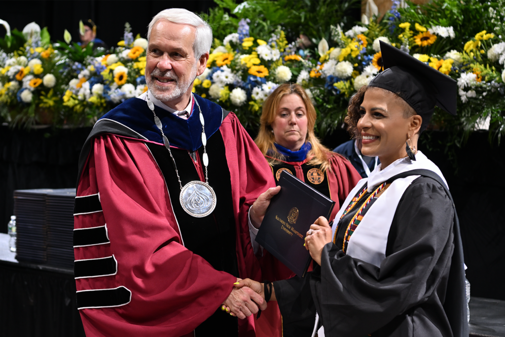 Tamica Matos接收她的文凭,脸上洋溢着微笑,握手SNHU总统勒布朗在她的毕业典礼。